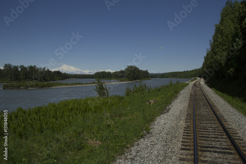 Railroad track running alongside a river with Denali in the background