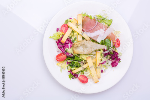European cuisine dish salad from vegetables, cheese and ham. food on a white plate and a top view of a light background
