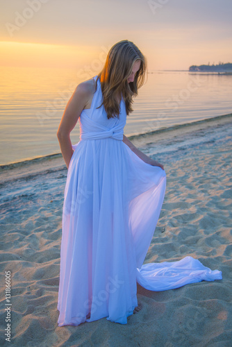 Beautiful girl in a long white dress walking on the seaside.