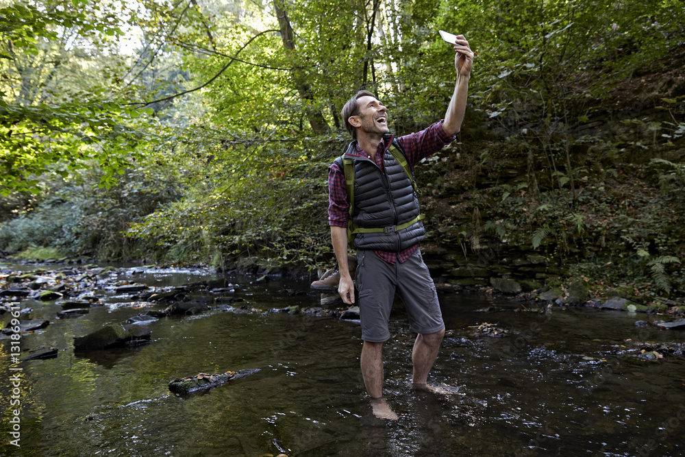 Hiker in forest standing at brook, taking selfie Hiker in forest standing at brook, taking selfie