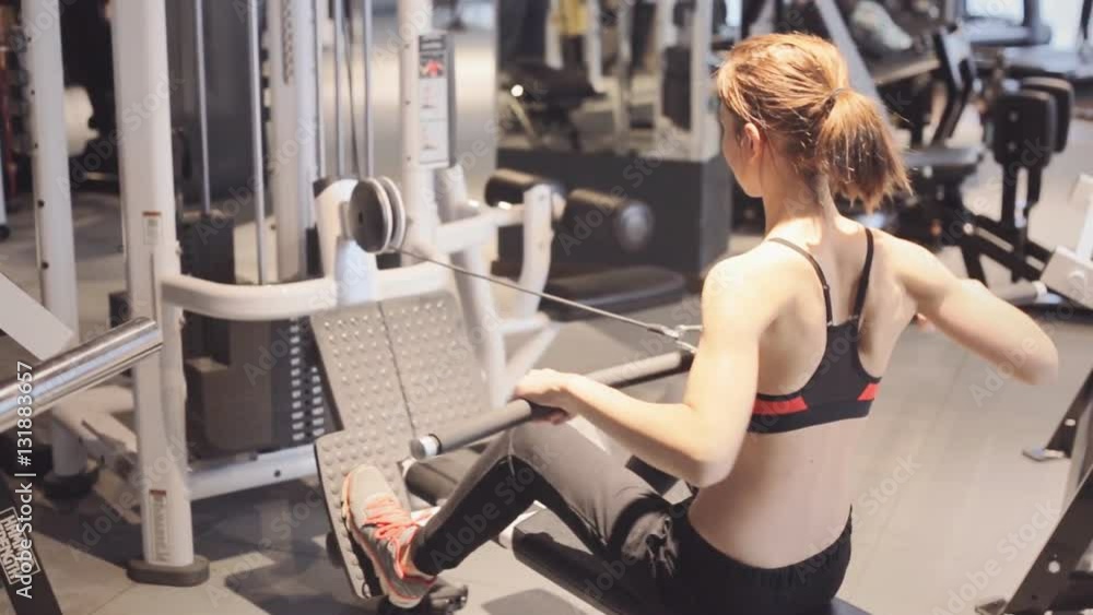 Athletic young woman doing a fitness workout in triceps simulator in gym Athletic young woman doing a fitness workout in triceps simulator in gym
