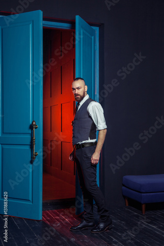 Stylish young fashion model in a suit near door with red light. Business style. Fashionable image. Evening dress. Sexy man standing and looking at the camera. Fashion look. 