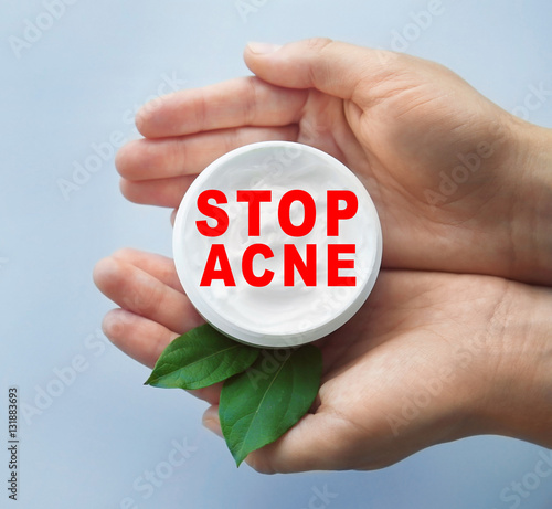 Female hands holding jar with facial cream. Text STOP ACNE on background