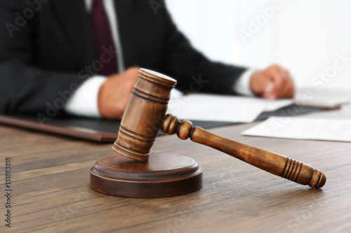 Brown gavel on wooden table and male lawyer on background, close up view