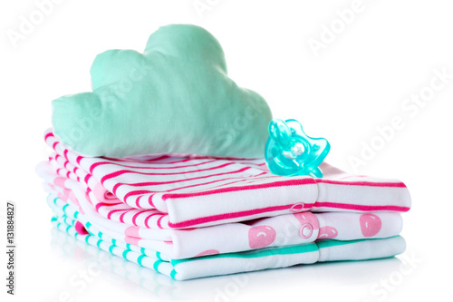 Pile of baby clothes, cushion and dummy on white background
