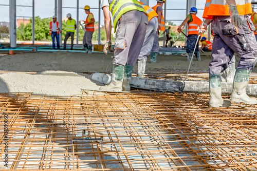 Workers are spreading concrete over big reinforced floor on the