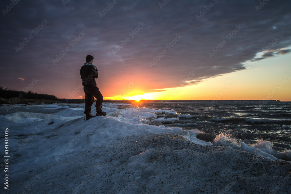Male Photographer Standing On A Frozen Lake. Single male photographer standing on the edge of a frozen lake during a beautiful winter sunset. Port Crescent State Park. Port Austin, Michigan.