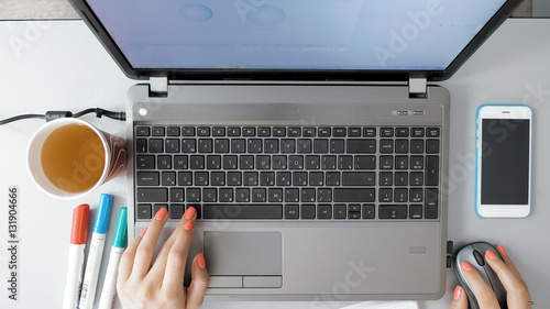 Female hands working on her laptop on graphic design. POV from first person. The smartphone paper cap and highlighters are shown on her desk. Modern computer technology has improved.