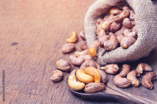 roasted cashew nuts with shell in gunny bag and on wooden spoon.