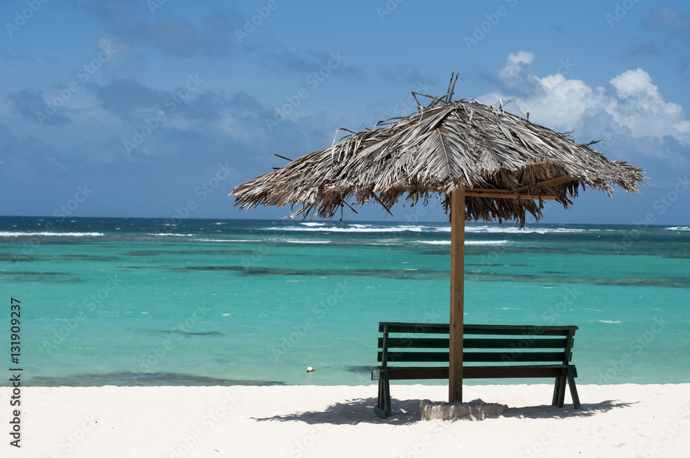 Fototapeta premium Empty bench on a sandy beach with a grass umbrella