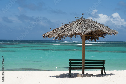 Empty bench on a sandy beach with a grass umbrella