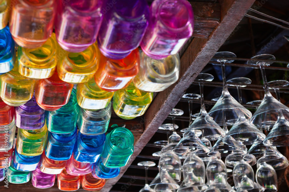 Restaurant interior background with narrow focus. Empty transparent wineglasses, rows of colorful beverage glasses hanging on top rack above bar counter. Vintage style wood ceiling.