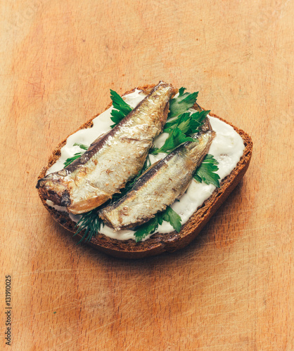 sandwich of canned sprats on rye bread with mayonnaise and parsley, and dill on a wooden cutting board close up