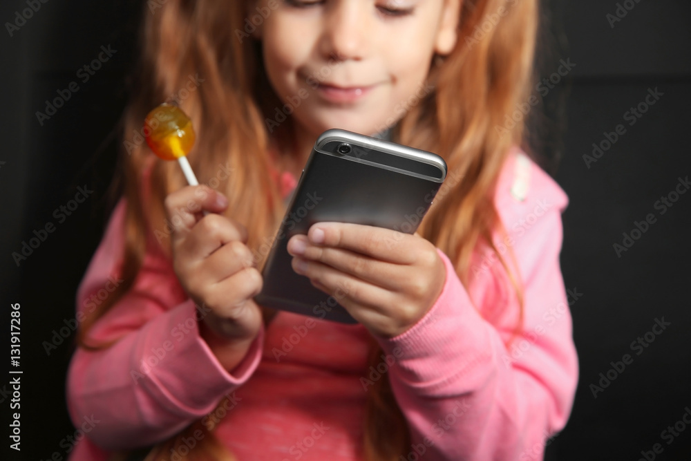 Fototapeta premium Little girl with lollipop using smartphone in a car