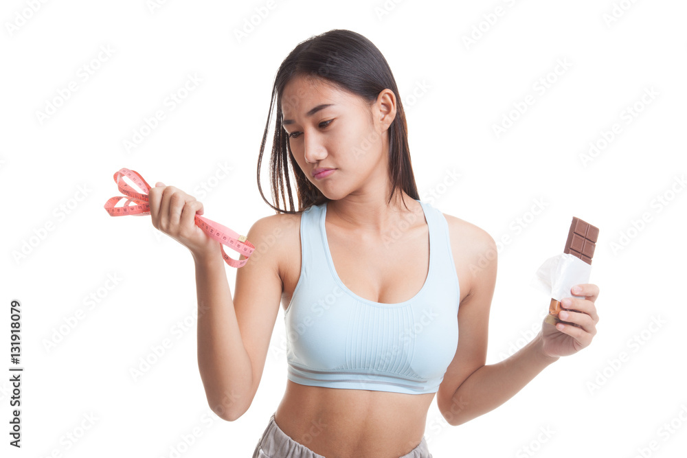 Unhappy Asian healthy girl with chocolate and measuring tape. Unhappy Asian healthy girl with chocolate and measuring tape.