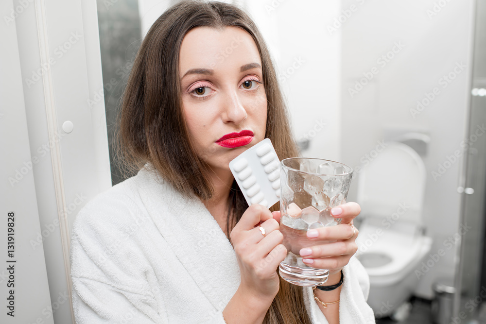 Sick woman with headache holding pills and glass of water in the bathroom Sick woman with headache holding pills and glass of water in the bathroom