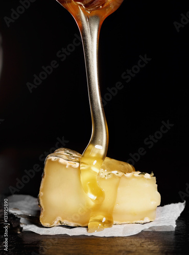 Slice of camembert with with honey (pouring from honey spoon).Black background