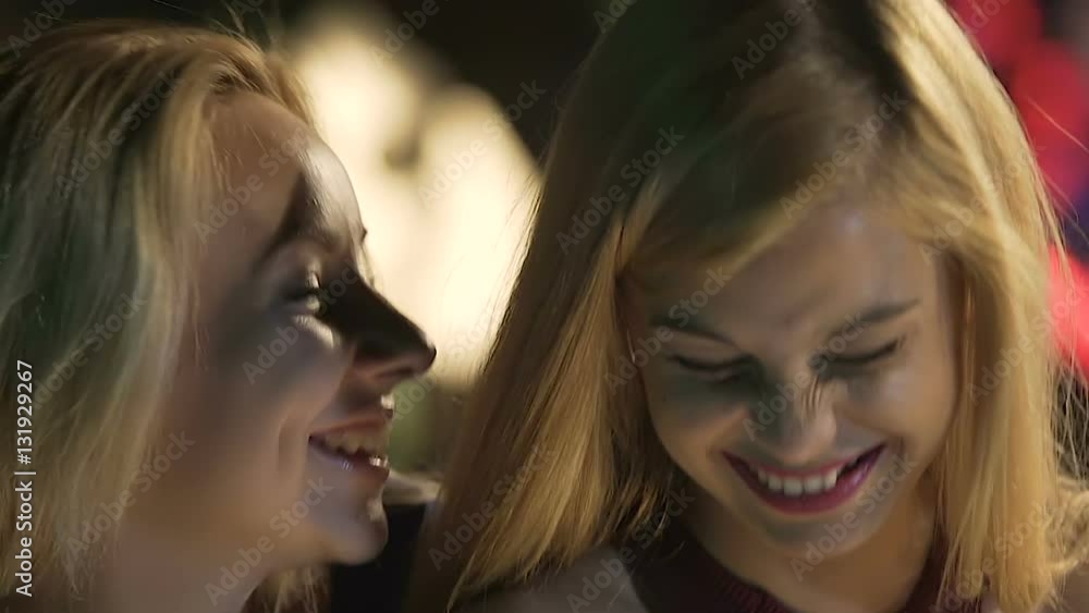 Two pretty girls typing and laughing at text message while drinking in nightclub Two pretty girls typing and laughing at text message while drinking in nightclub