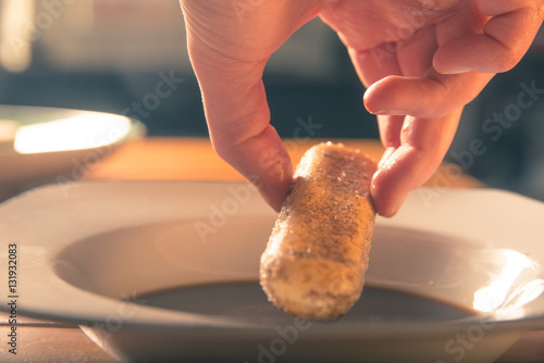 Hand dips a savoiardi biscuit into coffee