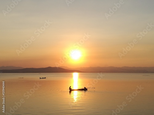 Silhouette view of beautiful sunset over the lake having boat in middle of sun reflection in summer