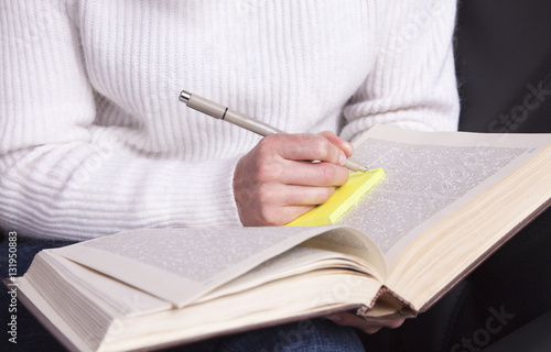 Girl with a book in hand taking notes with a pen.