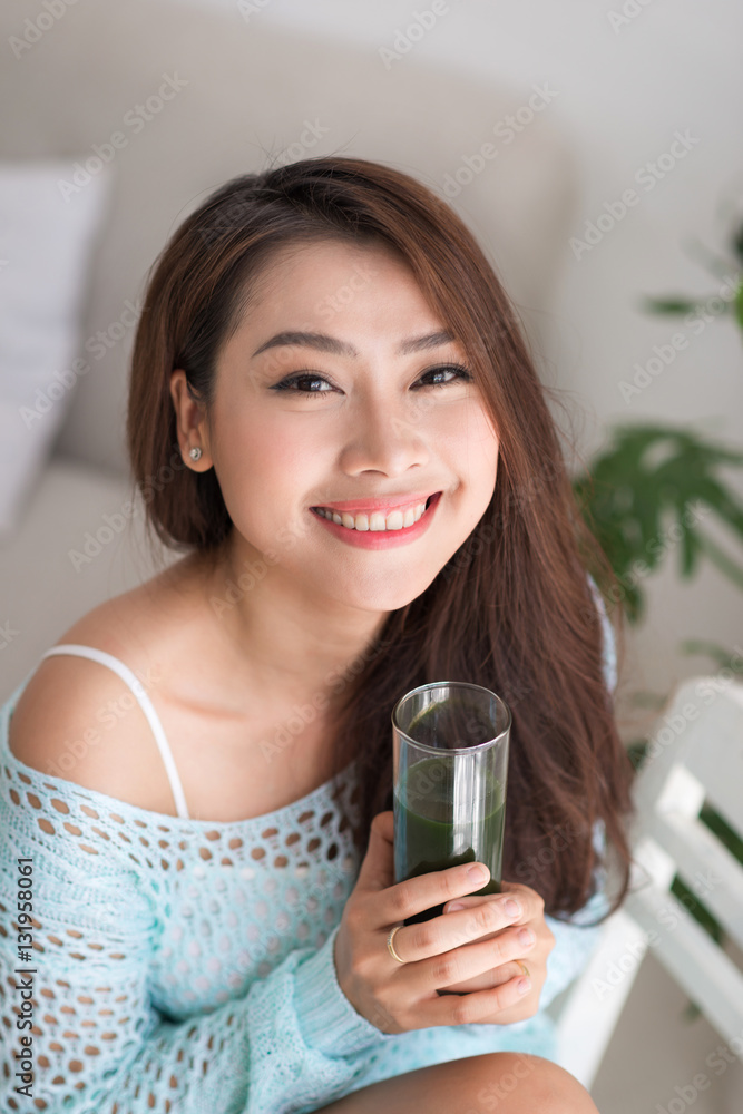 Smiling young asian woman drinking green fresh vegetable juice o Smiling young asian woman drinking green fresh vegetable juice o