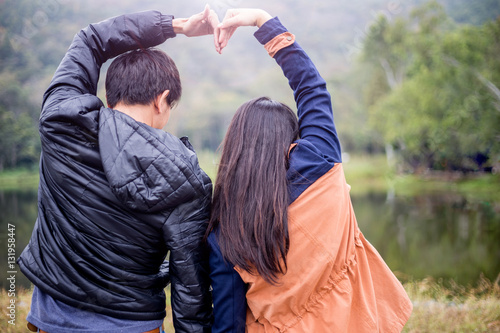 Couple makes heart shape with hands by lake in a park during late afternoon