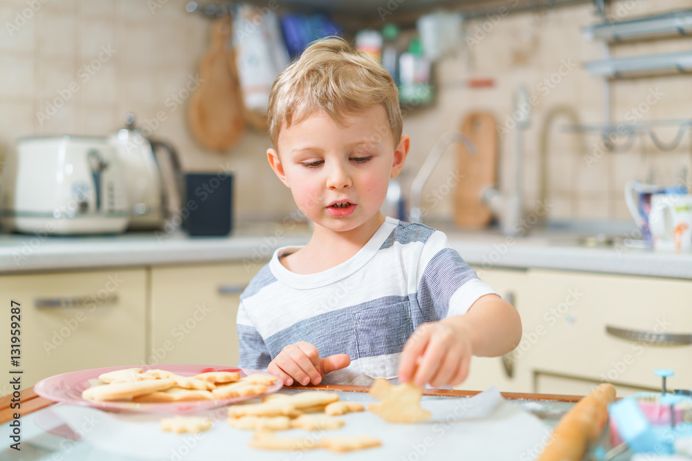 Little blond kid tries freshly baked shortbread, sitting at the kitchen table. Concentrated face expression. Little blond kid tries freshly baked shortbread, sitting at the kitchen table. Concentrated face expression.