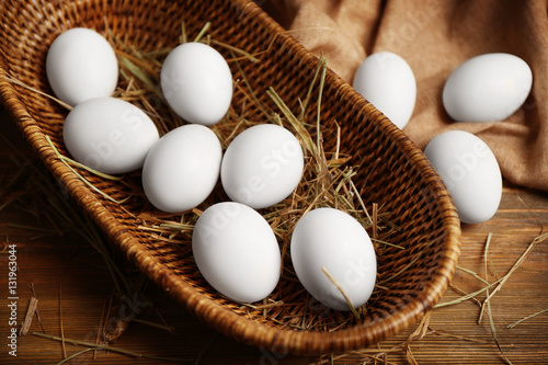 Raw eggs in basket on wooden background