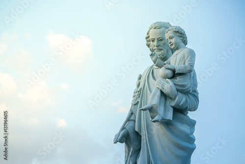 classical statue of Saint Joseph with child Jesus on blue sky.  Joseph is a figure in the Gospels  the husband of Mary   mother of Jesus and is venerated as Saint Joseph in the Catholic Church.  