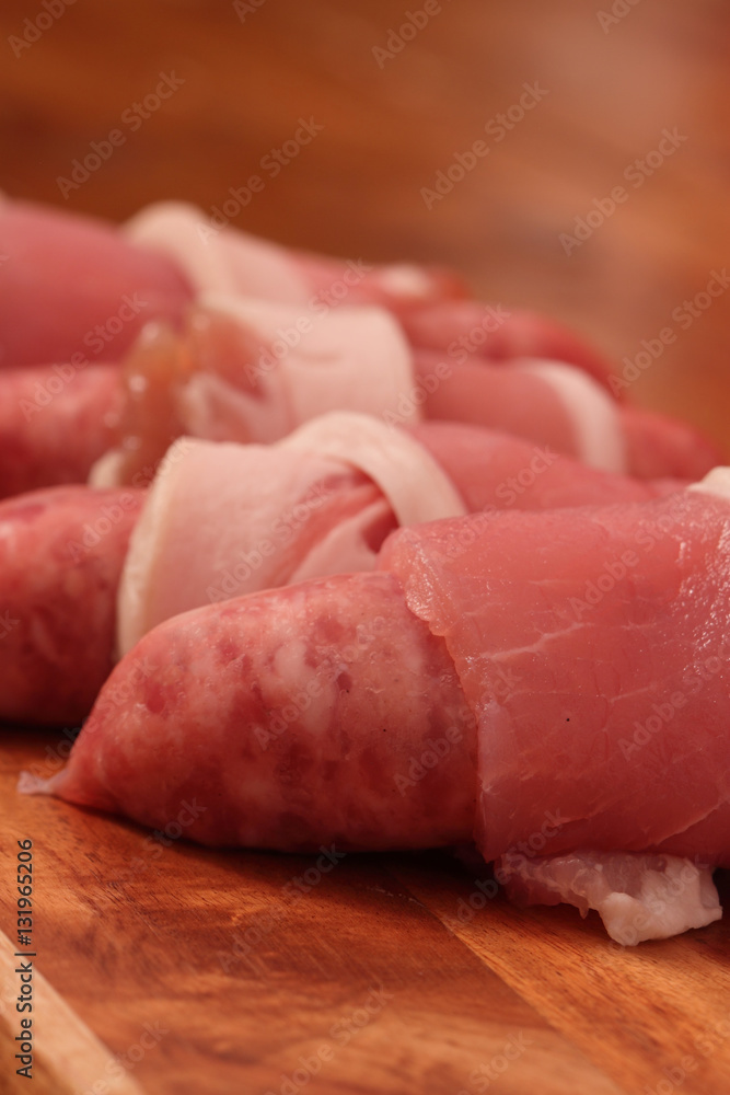 Raw sausages wrapped in bacon on a chopping board Raw sausages wrapped in bacon on a chopping board