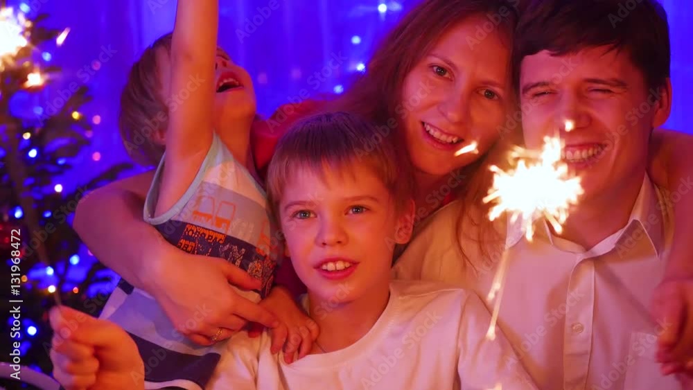 Happy family lit sparklers at the party. In the background, bokeh lights and garlands of Christmas fir Happy family lit sparklers at the party. In the background, bokeh lights and garlands of Christmas fir