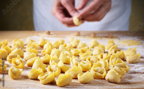 Man`s hands making tortellini on pastry board.