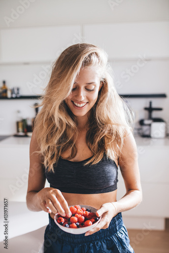 Happy young female in kitchen eating berries