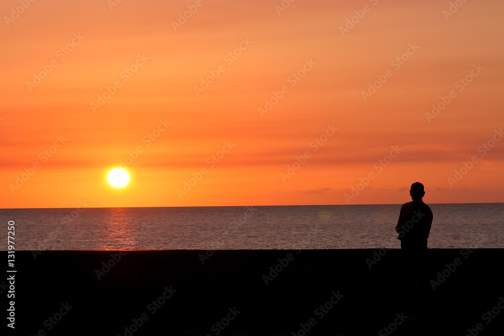 Silhouette of a man meditating in the sun on a background of sea sunset.