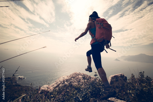 successful hiker jumping on seaside mountain peak rock