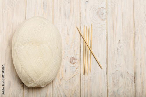 White yarn and wooden knitting needles on a light wooden backgro
