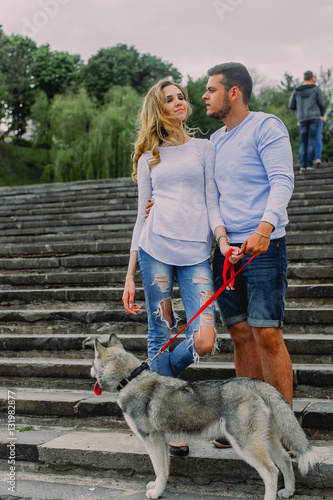 Beautiful young couple playing with a dog husky in a park. Summer outdoors. © dashamuller