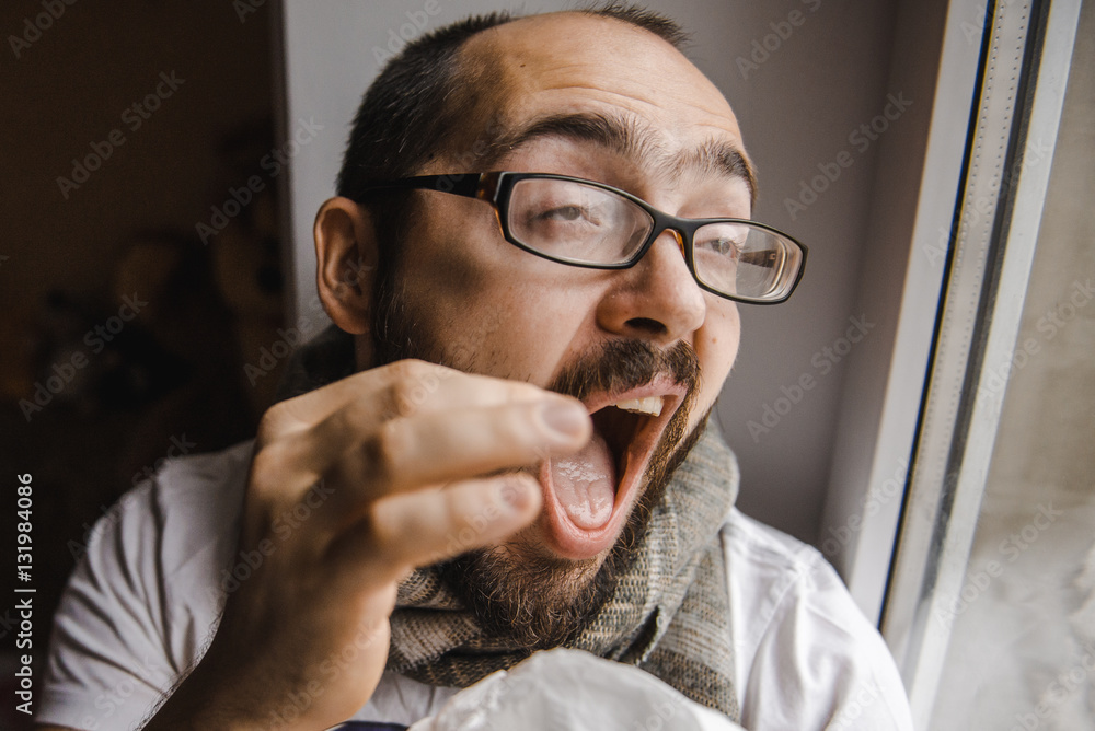 Young man blowing his nose while sitting at the window Young man blowing his nose while sitting at the window