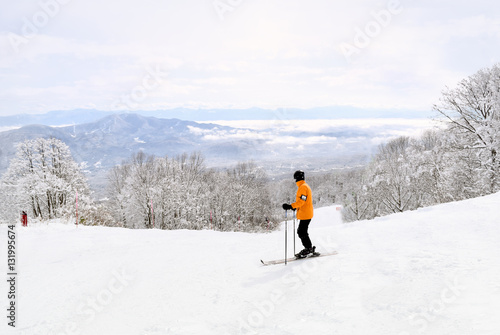 Skier taking in the beautiful Myoko scenery before continuing down the mountain. Distant mountain ranges are partially covered by low lying clouds.