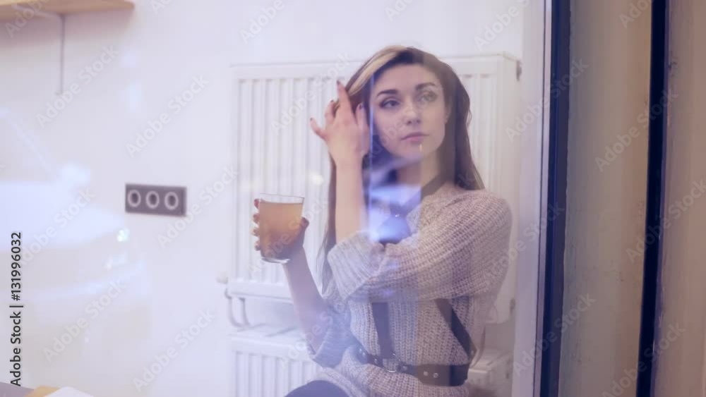 woman viewed through window drinks hot tea and takes her smartphone woman viewed through window drinks hot tea and takes her smartphone