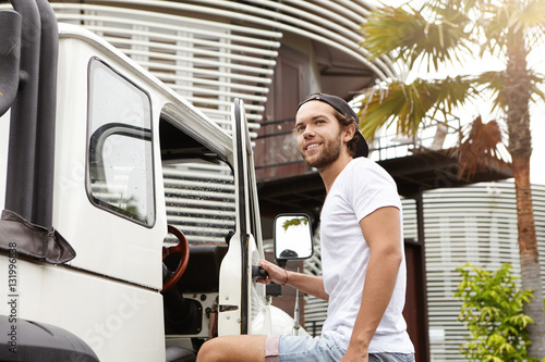 People, travel and adventure concept. Attractive man with beard smiling and saying goodbye to his friends after active weekend outdoors while standing outside his white jeep, ready to get into car