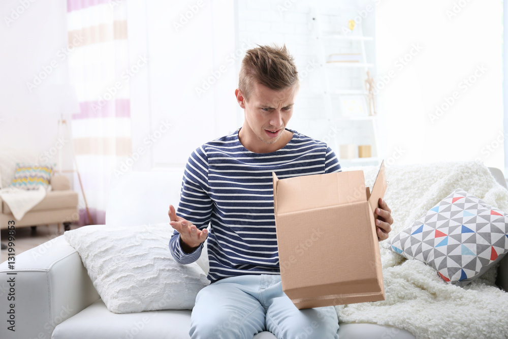 Young man sitting on sofa and unpacking received parcel Young man sitting on sofa and unpacking received parcel