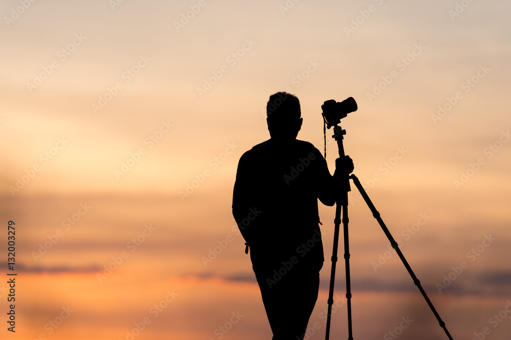 photographer silhouette with accessories and holding hand on tripod ,
taking pictures of the beautiful moments during the sunset ,sunrise