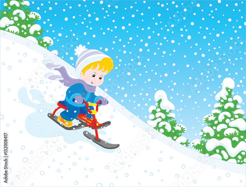Little boy sliding down the snow hill on his small snow-scooter