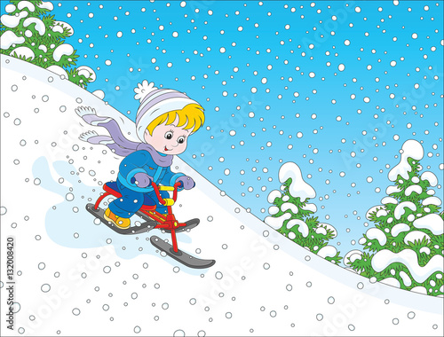 Little boy sliding down the snow hill on his small snow-scooter