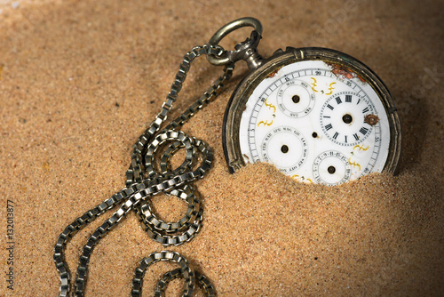 Old and broken pocket watch with chain partially buried in the sand