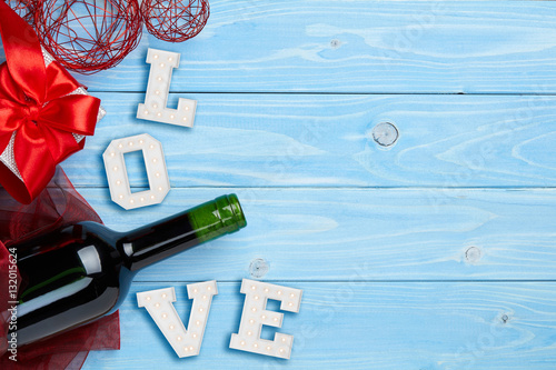 Composition of bottle of red wine on blue wooden background with gift and big love gign photo