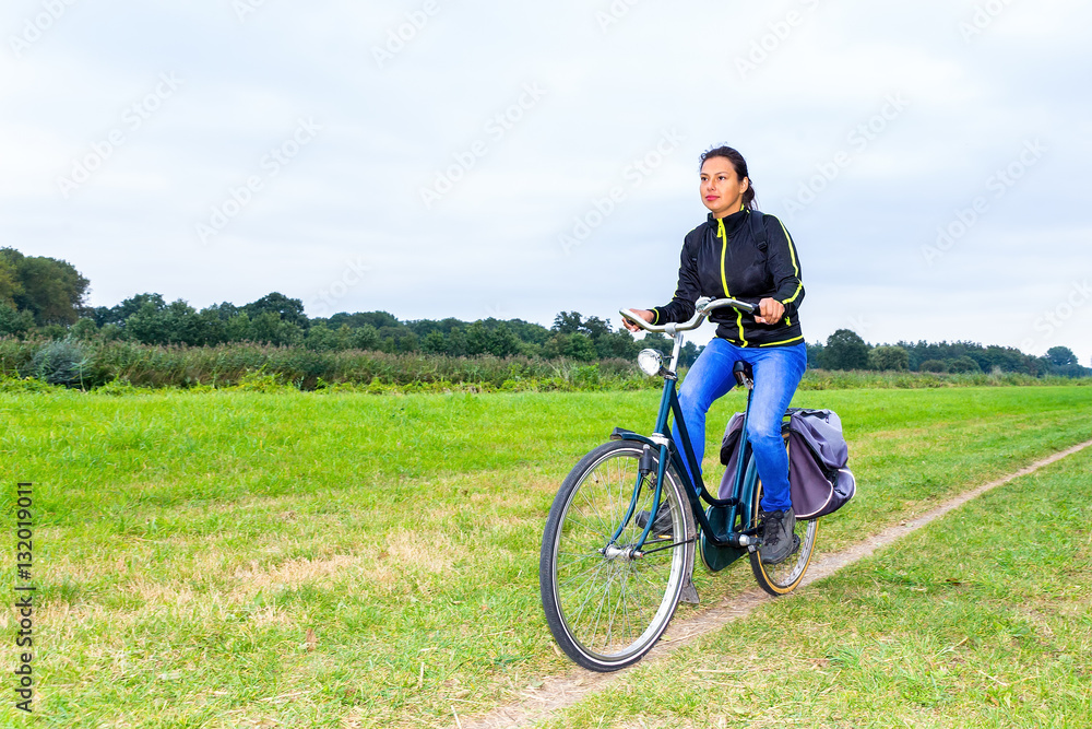 Colombian woman cycling on path in dutch nature landscape