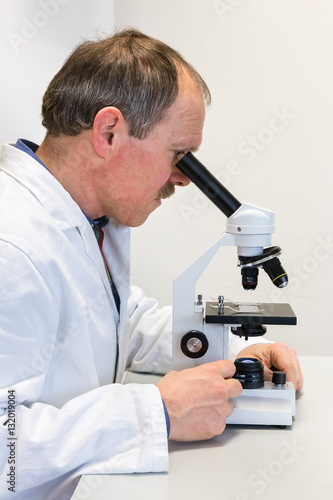 Biologist in lab coat looking through microscope